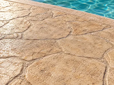 Pavimento de hormigón impreso con textura de losa de piedra y tonos arena junto a piscina